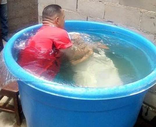 Una fotografía de un bautismo por inmersión en una bañera redonda muy grande en la que caben dos adultos.