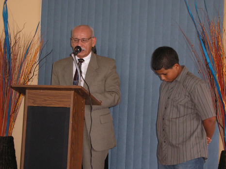 Hacía unos instantes antes de la toma de esta fotografía, el joven a la derecha confesó "con su boca que Jesús es el Señor". Dirigido por un anciano (obispo) de la iglesia, todos los congregados piden bendiciones divinas para el joven y su decisión sabia e importantísima de obedecer los mandamientos de Cristo. Terminada la oración, el joven fue bautizado "enseguida", glorioso acto registrado en la siguiente fotografía. 