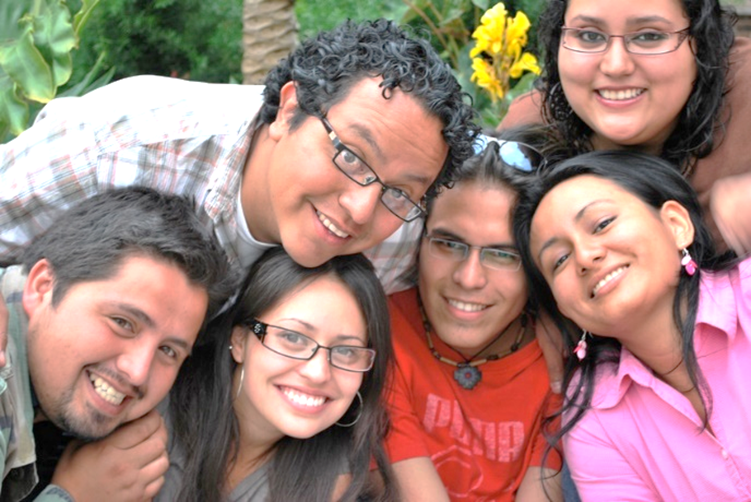 Un retrato de una familia latina de seis miembros, todos mirando de cerca a la cámara y sonriéndose de felicidad.