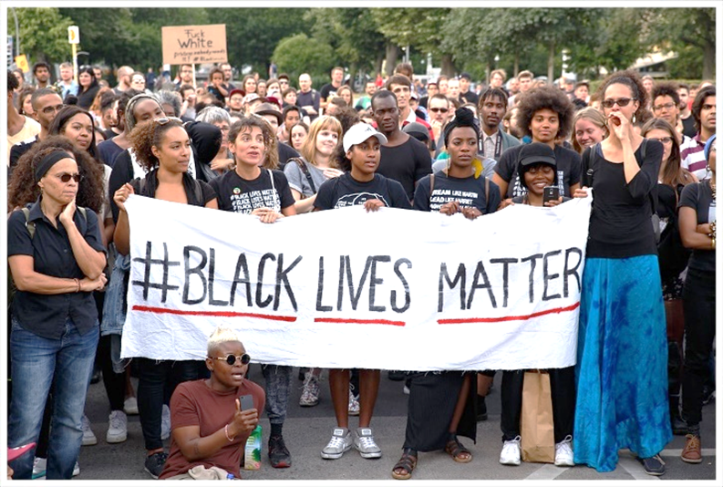 Una fotografía de una convocación de personas que respaldan el movimiento de Las vidas negras importan, sosteniendo las de primera plana una cartulina blanca con las palabras en inglés Black Lives Matter.