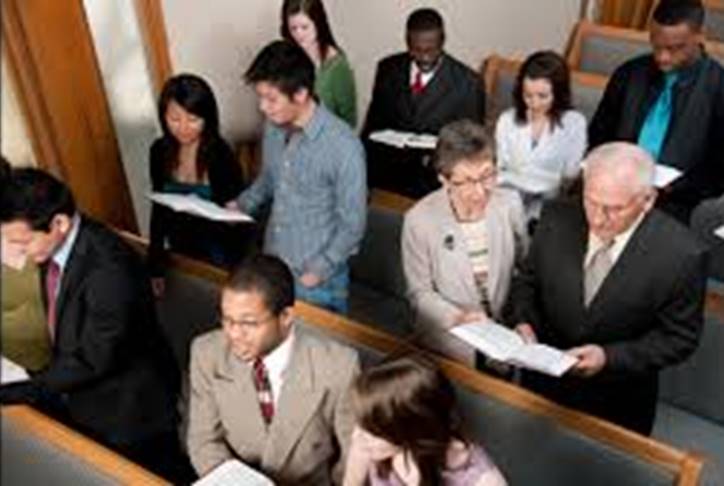 Una fotografía de un grupo de adultos de distintas razas en el acto de cantar himnos de alabanza en el lugar de reunión de una iglesia.